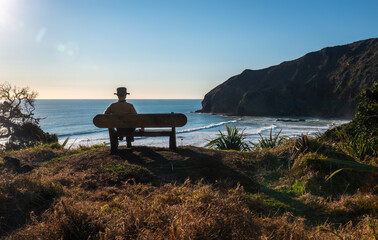 Fototapeta premium Man sitting on the bench and looking at the view at Bethells Beach. Waitakere. Auckland.