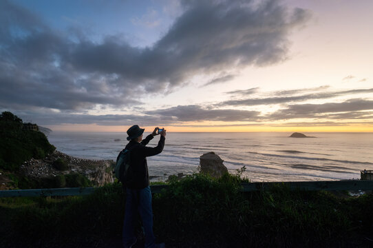 Man taking mobile phone photos at Muriwai Beach at sunset. Auckland.
