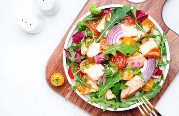 fresh salad with grilled salmon with tomato, cucumber, arugula, radicchio, red onion and lettuce with lemon oil dressing. Healthy delicious lunch. White table background, top view