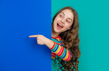 amazed teen child behind blank blue paper with copy space for advertisement. point finger