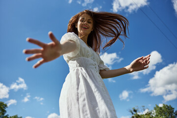 Fototapeta na wymiar happy red-haired woman offer one's hand her hand to the camera while standing against the background of a blue sky with clouds