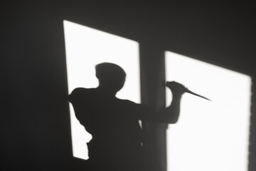 The shadow of a man holding a knife in his hand on a gray wall. The concept of danger, crime.