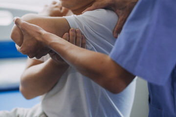 Doctor or Physiotherapist working examining treating injured arm of athlete male patient, stretching and exercise, Doing the Rehabilitation therapy pain in clinic.