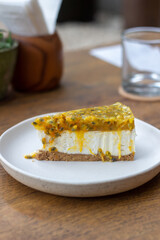 Close-up of a delicious cheesecake with fresh passion fruit topping on a plate on the table in a cafe. Vertical shot. Sweet dessert
