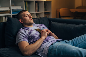 A caucasian man fell asleep on the couch with a mobile phone in his hands