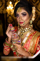 Magnificent young Indian bride in luxurious bridal costume with makeup and heavy jewellery holding...
