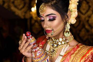 Magnificent young Indian bride in luxurious bridal costume with makeup and heavy jewellery holding...