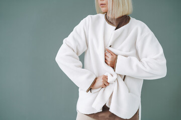 Crop portrait of young blonde woman in fleece jacket on background of grey wall