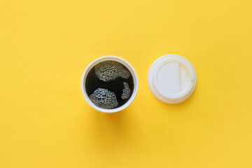 Glass of coffee to go with white plastic cap top view on yellow background