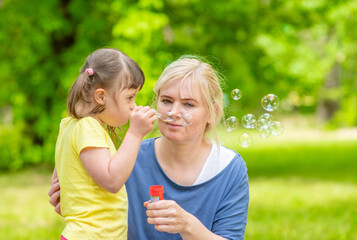 little girl with Downs syndrome and her mother blow bubbles at summer park