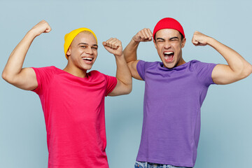 Young couple two friends men wear casual clothes look camera together showing biceps muscles on hand demonstrating strength power isolated on pastel plain light blue cyan background studio portrait
