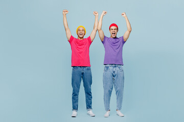 Obraz premium Full body excited happy cool young couple two friends men wear casual clothes together do winner gesture clench fist raise up hands isolated on pastel plain light blue cyan background studio portrait.