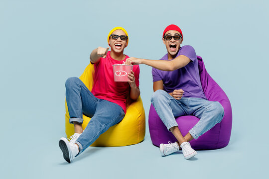 Full body young couple two friends men wearing casual clothes in 3d glasses watch movie film hold bucket of popcorn in cinema sit in bag chair point finger camera on you isolated on yellow background.