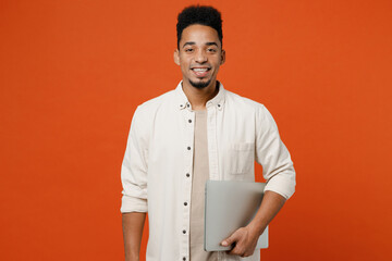 Young happy student IT man of African American ethnicity wears light shirt casual clothes hold cloed laptop pc computer chatting isolated on orange red background studio portrait. Lifestyle concept.