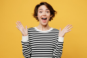 Young european surprised shocked amazed woman wear casual striped black and white shirt look camera spread hands say wow isolated on plain yellow color background studio portrait. Lifestyle concept.