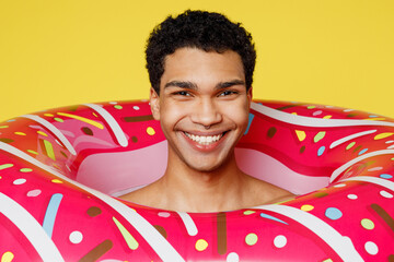 Close up handsome smiling cheerful fun young sexy man wear swimsuit rubber donut ring relax near hotel pool look camera isolated on plain yellow background. Summer vacation sea rest sun tan concept.