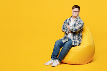 Full body young man with down syndrome wear glasses casual clothes sit in bag chair look camera...