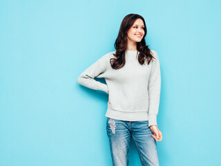 Young beautiful smiling female in trendy summer jeans and warm winter sweater clothes. Sexy carefree woman posing near blue wall in studio. Positive model. Cheerful and happy. Isolated.