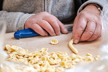 Wrinkled hands of an elderly woman preparing fresh orecchiette or orecchietta, made with durum wheat and water, handmade pasta typical of Puglia or Apulia, a region of Southern Italy, close up