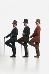 Portrait with three men wearing old-fashioned clothes and standing in a row over white background....