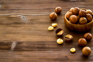 Wooden bowl of raw macadamia nuts in shell. Healthy protein snack background