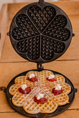 An antique waffle iron with a freshly baked crispy waffle, decorated with cream and raspberry jam