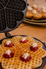 An antique waffle iron with a freshly baked waffle in it decorated with raspberry jam and cream
