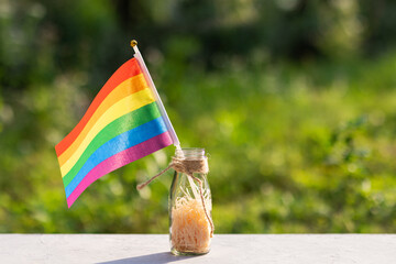 rainbow flag in glass on green bokeh background outdoor. celebrating pride month during Covid-19 Coronavirus pandemic quarantine, social distancing concept