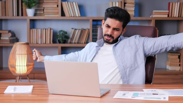 Overworked bearded man experiencing severe pain in neck at workplace. Man touches massages his neck, making constrained head movements. Condition caused by degenerative changes in the cervical spine. 