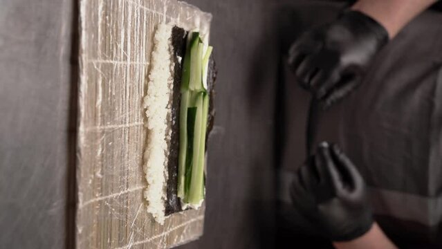 Preparing sushi. Chef preparing delicious sushi in a restaurant. Salmon, cucumber, rice on seaweed on steel table.