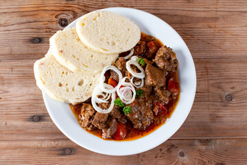Beef goulash with bread dumplings and parsley garnish on white ceramic plate on table. Top view.