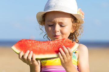 cute little girl eats ripe juicy red watermelon on the beach, coast, seashore. the concept of summer kid holidays, seasonal fruits and berries. closeup portrait