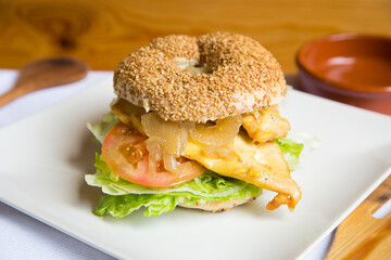 Delicious chicken sandwich on bagel bread. A bagel is a bread traditionally made from wheat flour and usually has a hole in the center.