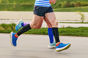 Plakat legs two male runners in compression socks and sleeves run marathon distance, endurance sports competition