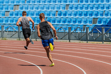 back two decathlon athletes running sprint race track, summer athletics championships at stadium