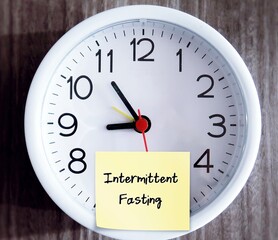 Wall clock with sticky note written INTERMITTEN FASTING, eating plan that switches between fasting...