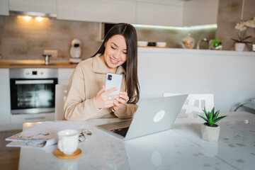 One young woman caucasian working at home in the kitchen and using a mobile phone, reading messages, modern lifestyle and business concept 