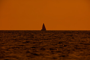 Fototapeta na wymiar Silhouette of a sailing boat in sunset sunrise time and ocean horizon.