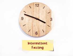 Wall clock with sticky note written INTERMITTEN FASTING, eating plan that switches between fasting...
