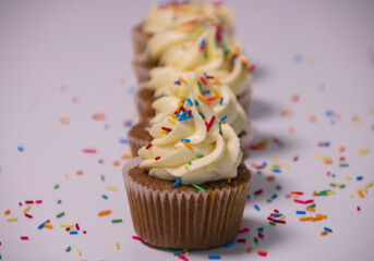 Cupcake with rainbow sprinkles vin symmetry, with the first cupcake in focus while those that follow are blurred.