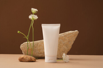 Minimal concept with stones and flower and white plastic bottle without label on brown background. Mockup for cosmetic product, facial moisturizer cream or facial cleanser. Front view