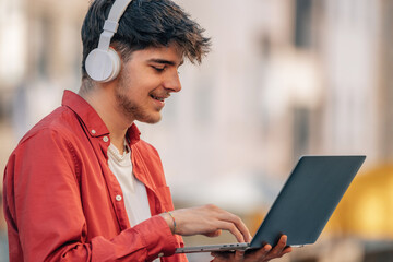 young male with headphones and laptop in the street