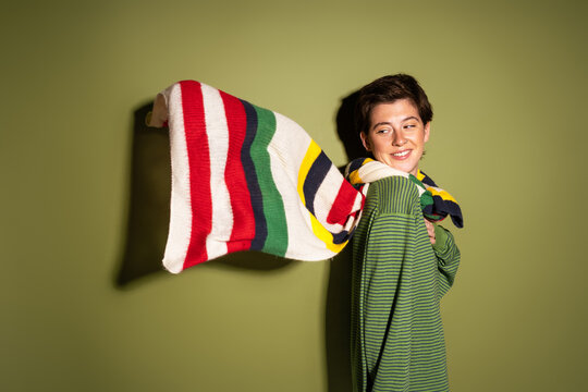cheerful woman looking at striped multicolored scarf waving on wind on green background.