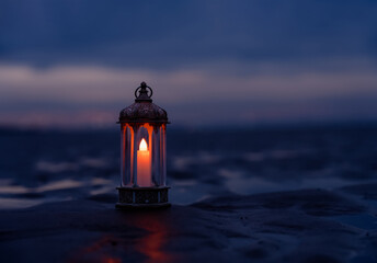Ramadan Kareem, Arabic lantern with burning candle on sand beach with blurry sunset sky...