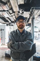 Fototapeta na wymiar Caucasian mechanic with glasses holding notes from car's inspection and looking at the camera, medium vertical shot. High quality photo