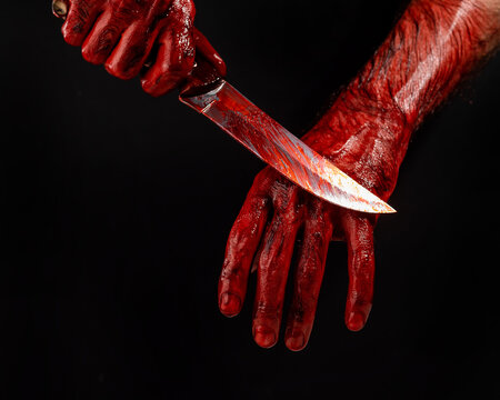 A man wipes a bloody knife with his hand on a black background. 