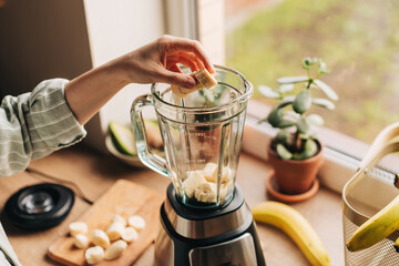 Woman is preparing a healthy detox drink in a blender - a green smoothie with fresh fruits, green spinach and avocado. Healthy eating concept, ingredients for smoothies on the table, top view