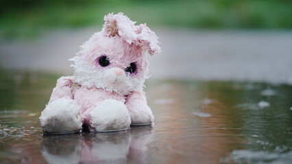 A cute toy rabbit is sitting in a puddle in the rain