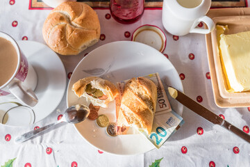 Gedeckter Frühstückstisch mit Frühstück aus Kaffee Zucker Milch und Butter und mit Euro Münzen und Geldscheinen belegtes Brötchen auf dem Teller, Deutschland