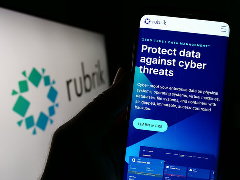 Stuttgart, Germany - 03-30-2023: Person holding cellphone with webpage of US data security company Rubrik Inc. on screen in front of logo. Focus on center of phone display.